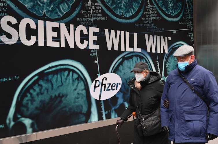 And older couple wearing a face masks walks past the Pfizer Inc. headquarters in New York City.