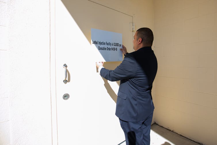 Man stands next to a sign reading that the lethal injection facility is closed due to COVID-19.