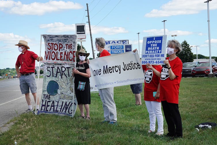 Half a dozen people hold anti-death penalty signs on a highway.