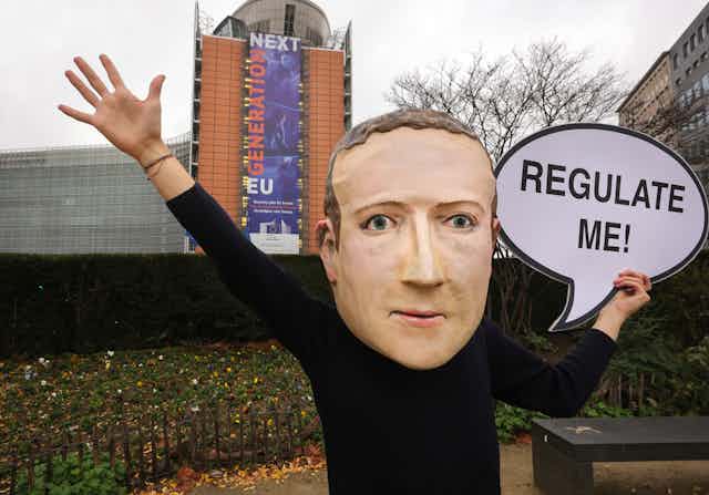 A campaigner from the global citizens movement Avaaz wearing a mask of Facebook CEO Mark Zuckerberg holds a sign reading "Regulate me" outside the European Commission