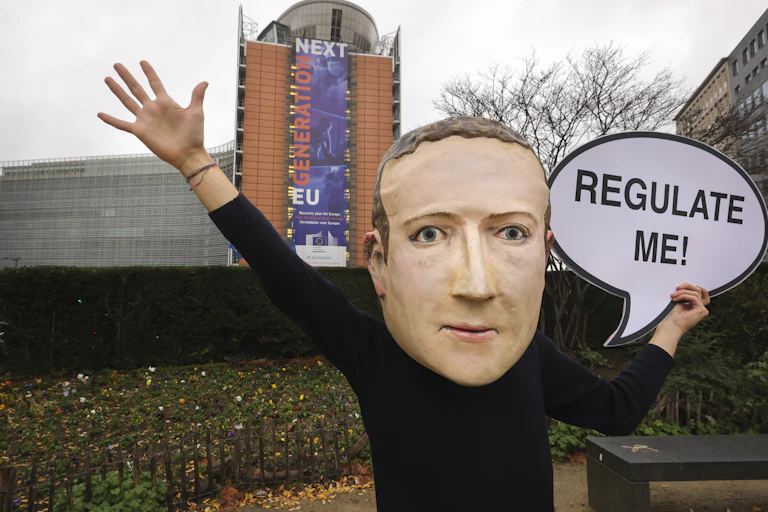 A campaigner from the global citizens movement Avaaz wearing a mask of Facebook CEO Mark Zuckerberg holds a sign reading "Regulate me" outside the European Commission