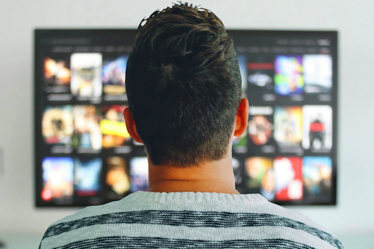 Un hombre de espaldas ante un televisor con una oferta variada.
