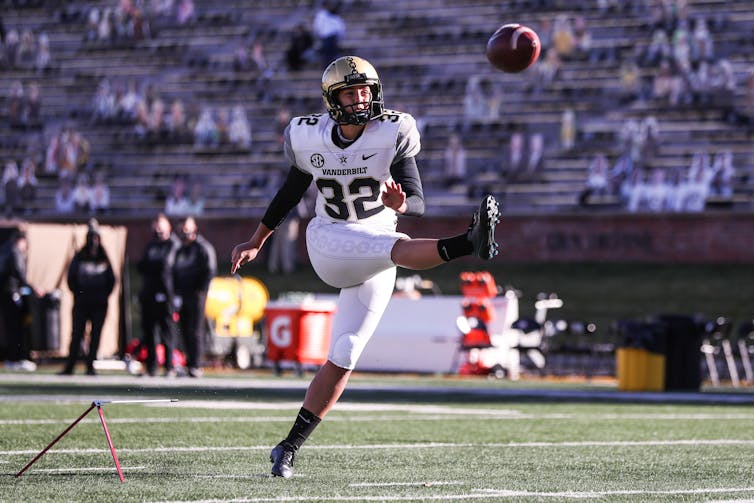 Uniformed football player kicks ball in the air