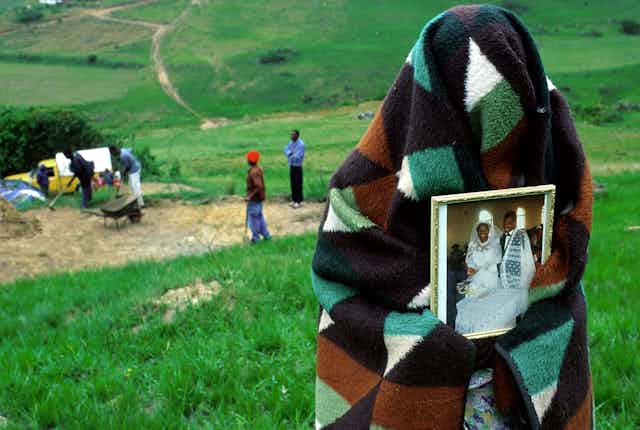 A woman covered with a blanket holds a photo of her and her dead husband on their wedding day.