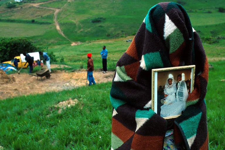 A woman covered with a blanket holds a photo of her and her dead husband on their wedding day.