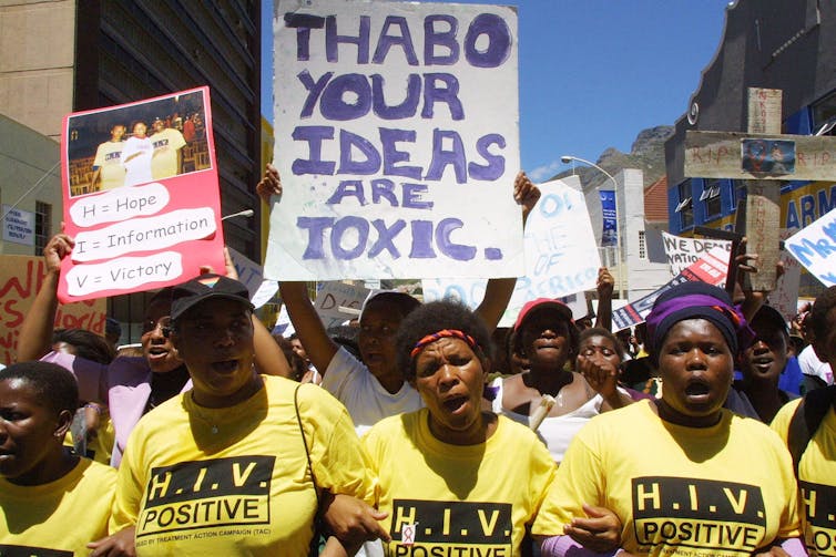 AIDS activists lock arms and hold anti-Thabo Mmbeki signs.