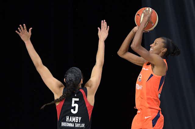 One woman basketball player tries to block another as she takes a shot.