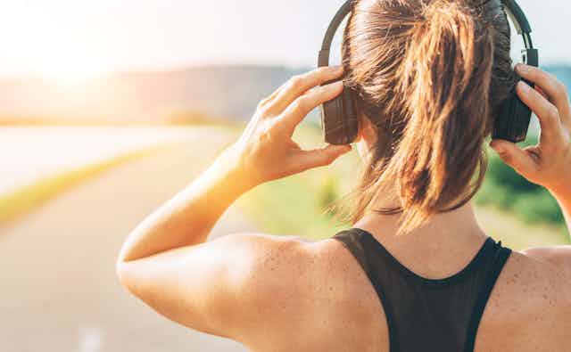Female runner adjusts headphones with road ahead.