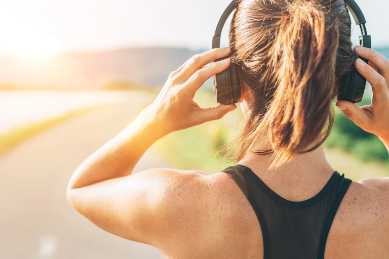 Female runner adjusts headphones with road ahead.