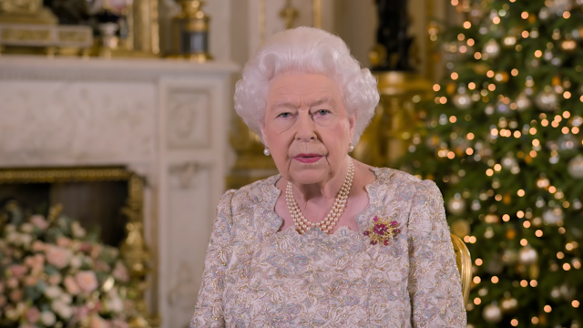 Queen Elizabeth II in a white top in front of a Christmas tree