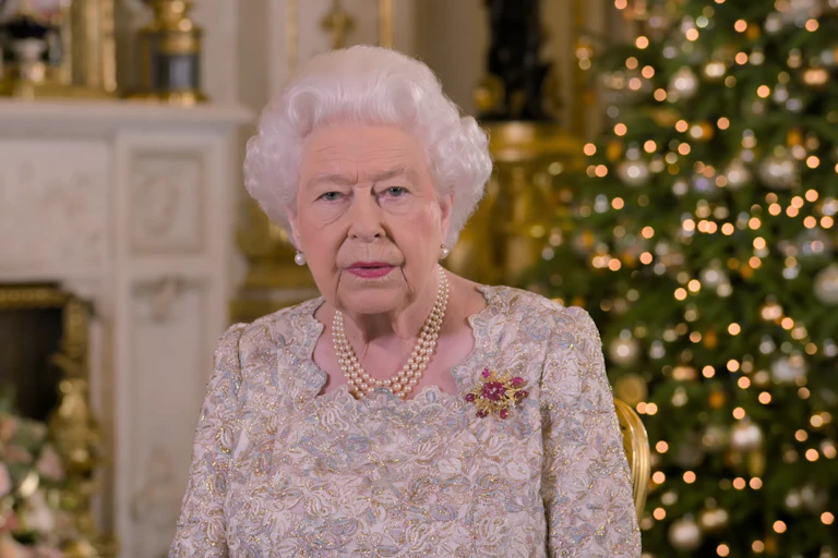 Queen Elizabeth II in a white top in front of a Christmas tree