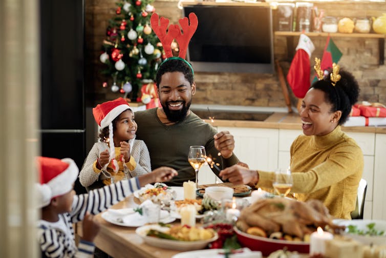 Joyful African American family using sparklers while having lunch and celebrating Christmas at dining table.