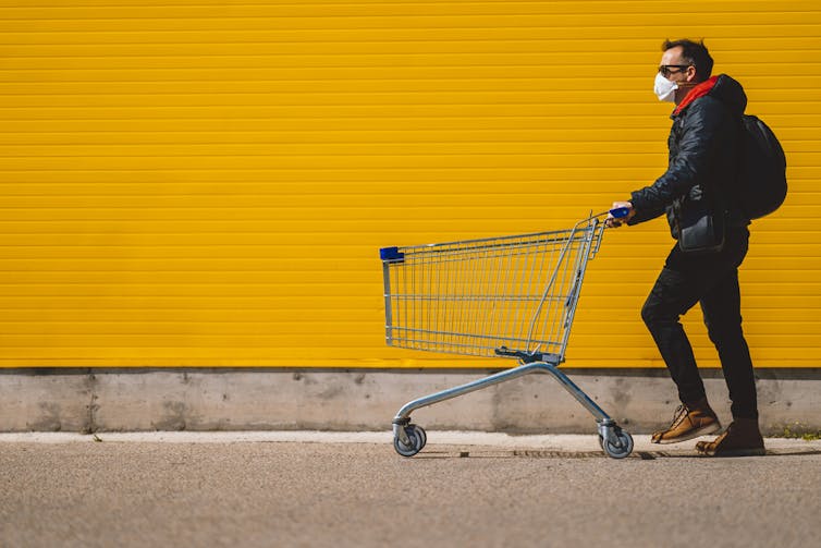 A man in a mask pushing a shopping trolley