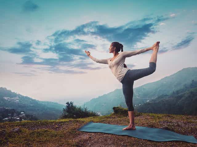 Woman practising yoga on a hillside.