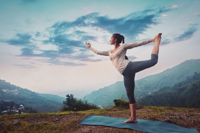 Woman practising yoga on a hillside.
