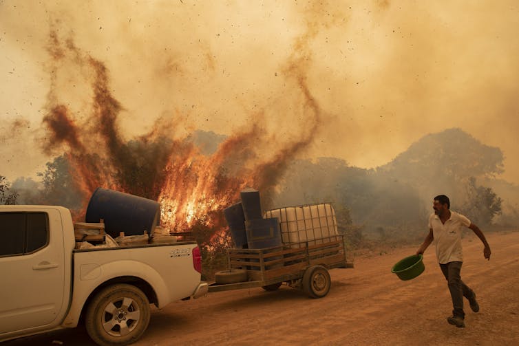 A man running with a bucket near a fire and a pickup truck.
