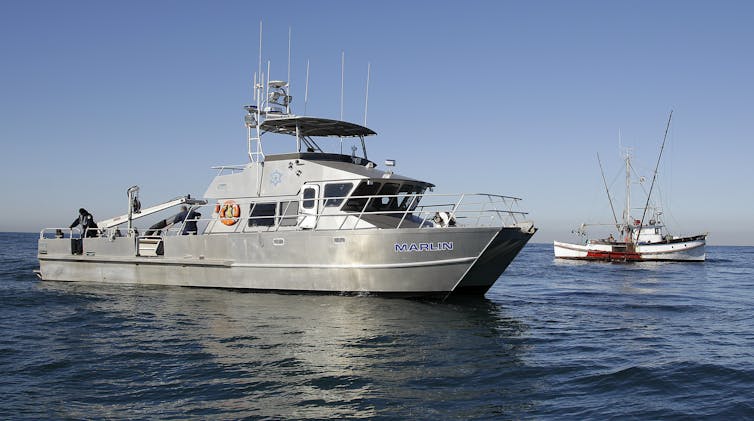 A California game warden boat next to a fishing boat.