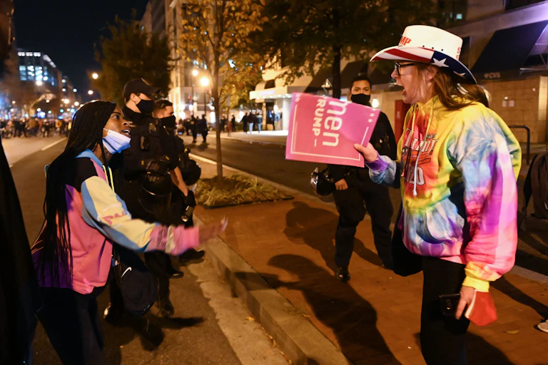 Young black woman and older white person in a cowboy hat yelling, at night