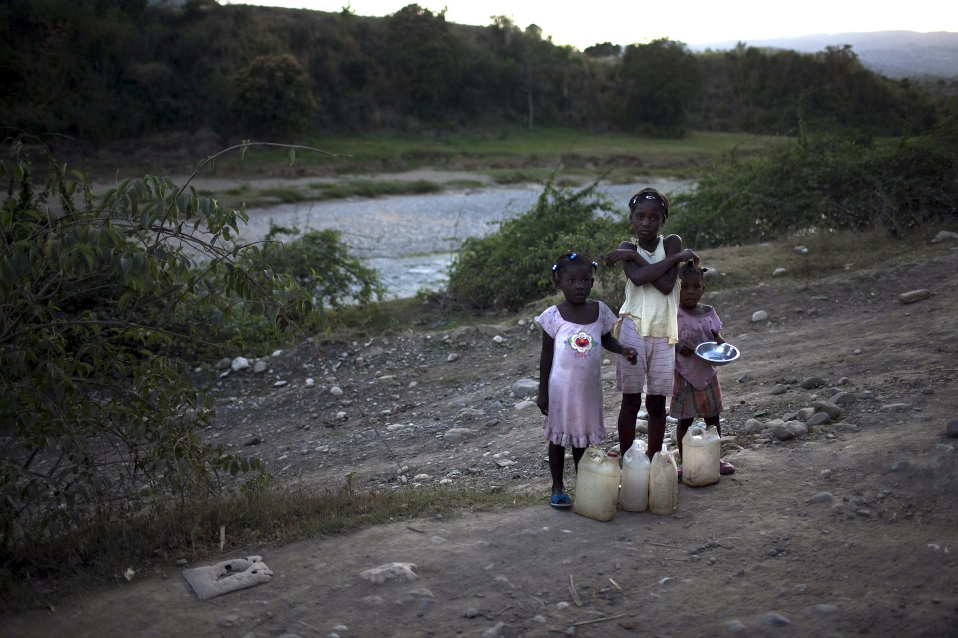 Drei junge Mädchen stehen am Rande eines Feldes in Haiti.