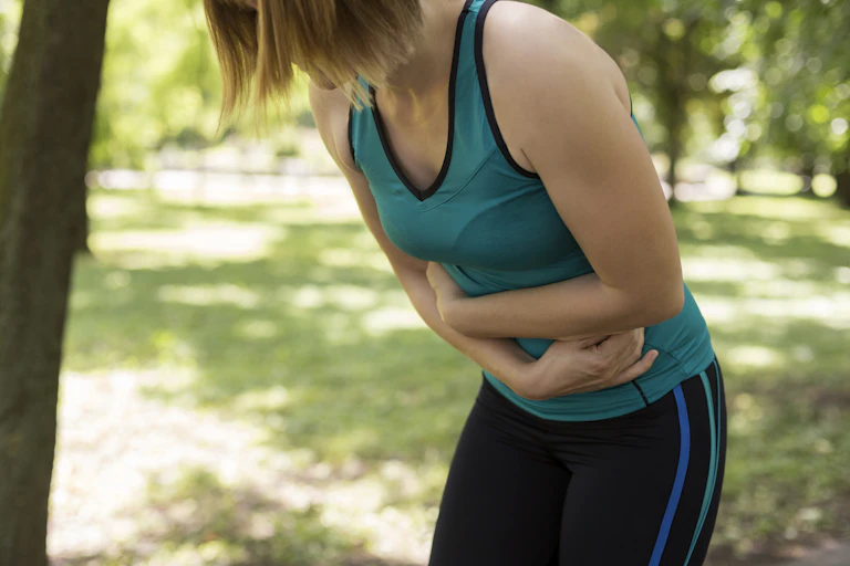 woman in exercise clothes holds belly and leans forward