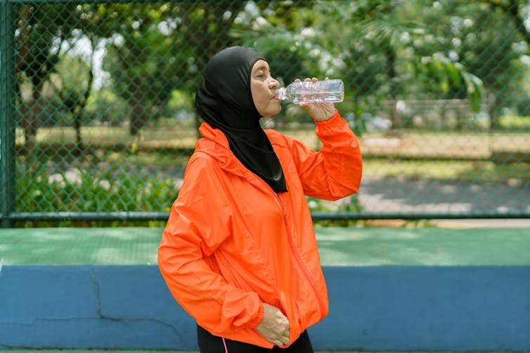 mujer en hijab bebe agua después del deporte