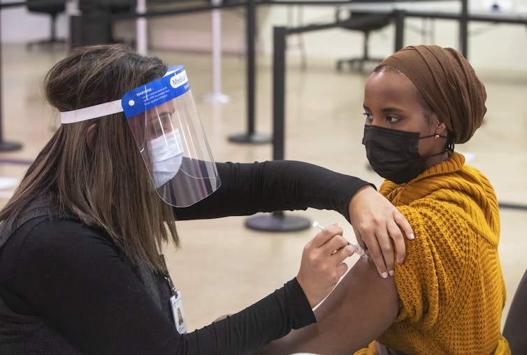 A nurse wearing a face visor vaccinates a woman wearing a face mask.