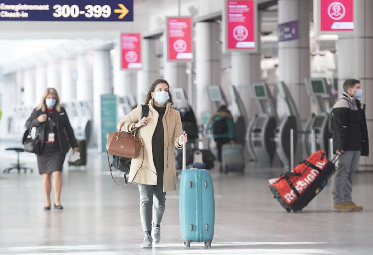 People in masks walk through an airport.