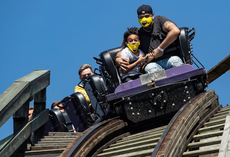 A man and child wearing masks ride a roller-coaster.