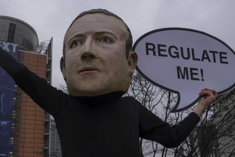 A person in an oversized mask of Mark Zuckerberg holds up a sign outside the European Commission offices in Brussels in December 2020 with a sign saying "regulate me"