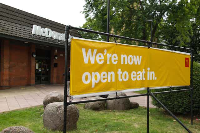A sign outside McDonalds say the restaurant is open for people to eat inside