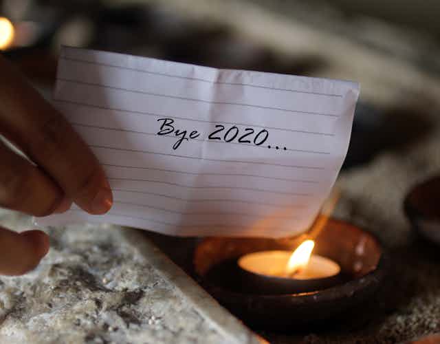 A piece of paper reading 'Bye 2020' held to a flame