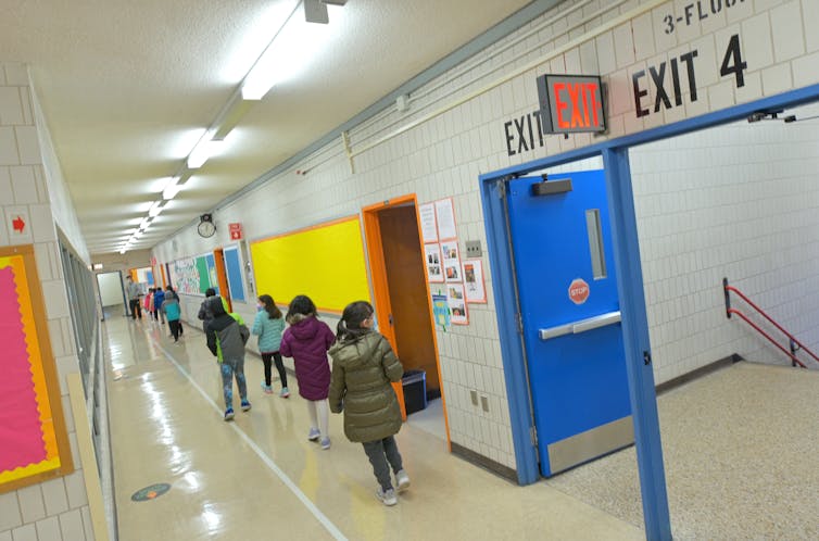 Children walk in single file down a school hallway