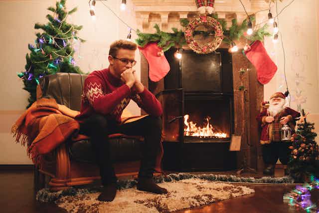 A man sits in a chair next to a fireplace surrounded by Christmas decorations.