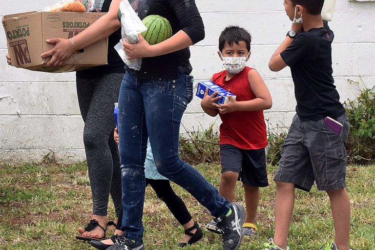 Two boys and two women carry food in a box and in their arms.