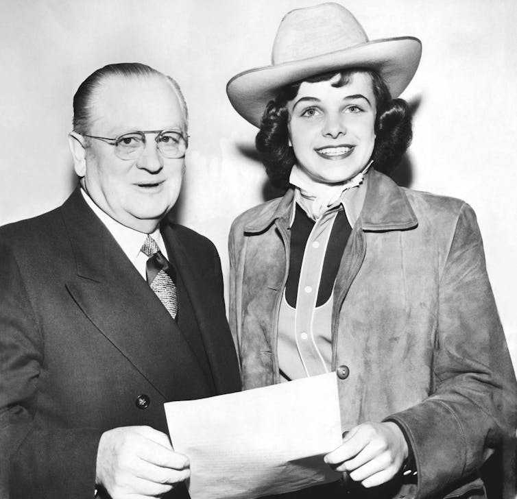 Black and white image of a young Feinstein in a cowboy hat standing next to an older man