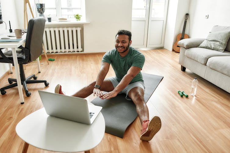 A man on an exercise mat in front of a laptop, with weights and a bottle of water beside him
