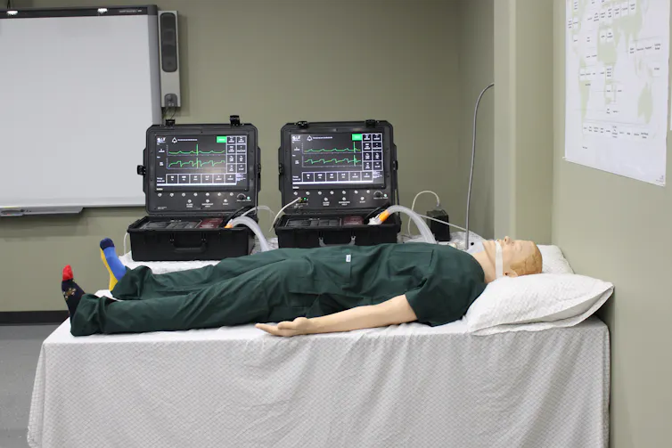 A medical dummy lying on a table with two ventilators behind it.