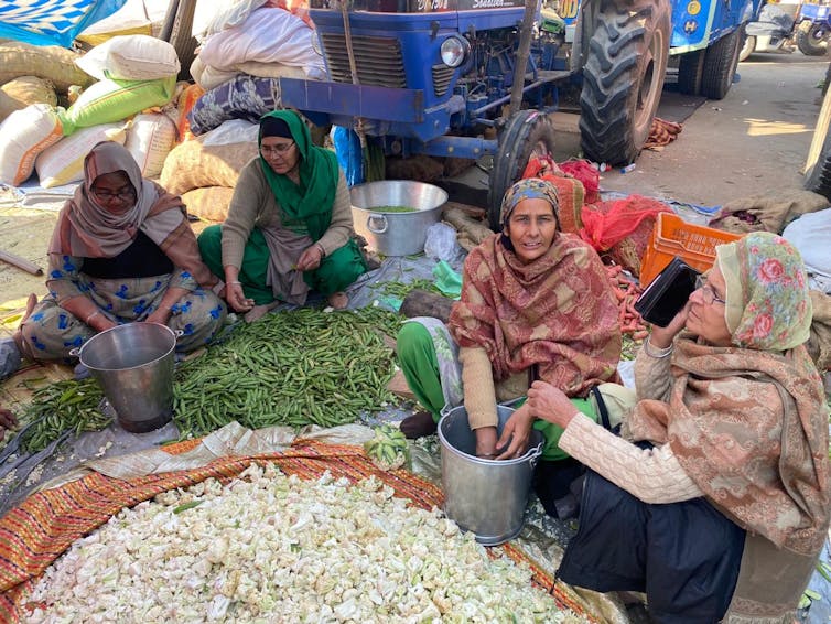 Four women are seen seated on the ground sorting through vegetables.