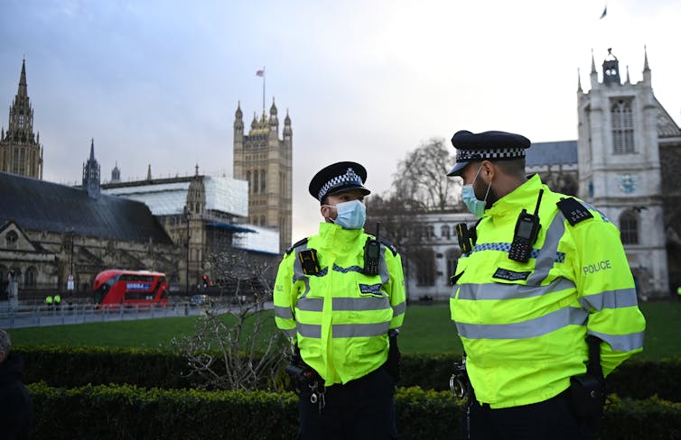Two police officers wearing face masks standing outside with parliament in the background