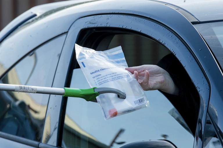 A person receiving a COVID testing kit through their car window