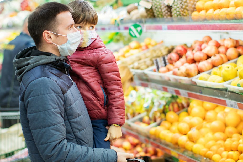 Father and son doing grocery in the supermarket wearing protective masks.