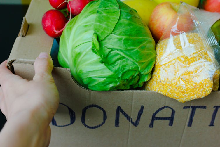 Support Food Banks During Coronavirus. COVID-19 Relief Funds and Donations. Volunteer in the Protective Medical Mask and Hand Gloves Holding Food Donation Box. Charity donations