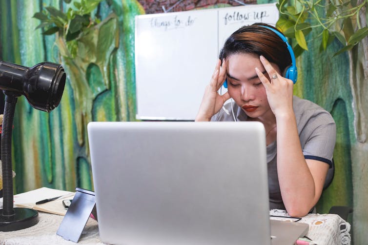 Young woman working at a laptop massages her temples.