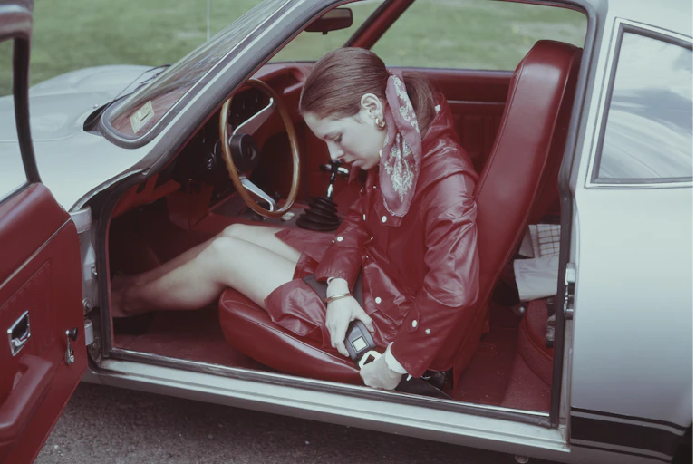 A 1960's era woman is fastening her seatbelt in a sporty car.