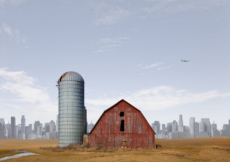 A barn in a field with a city in the background.