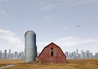 Eine Scheune auf einem Feld mit einer Stadt im Hintergrund.