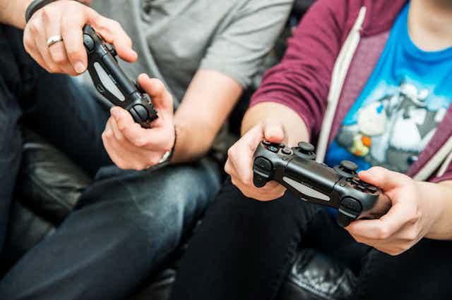 Man and young adult hold video game console controllers