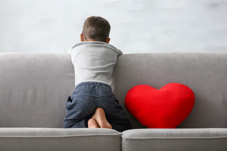 A boy faces a wall sitting on a couch.