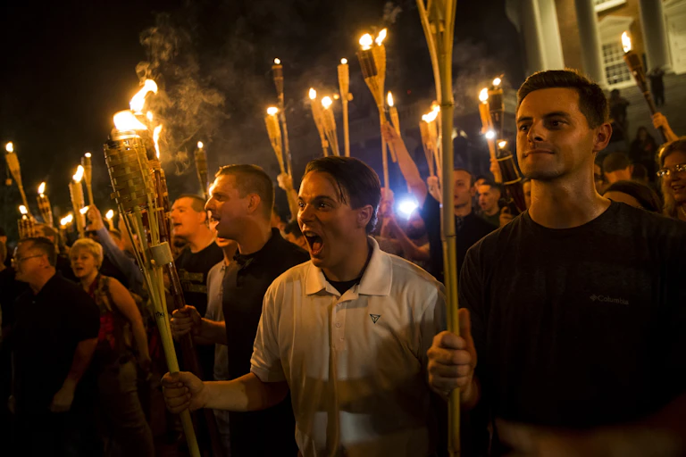 Crowd of men and women shout while holding tiki torches