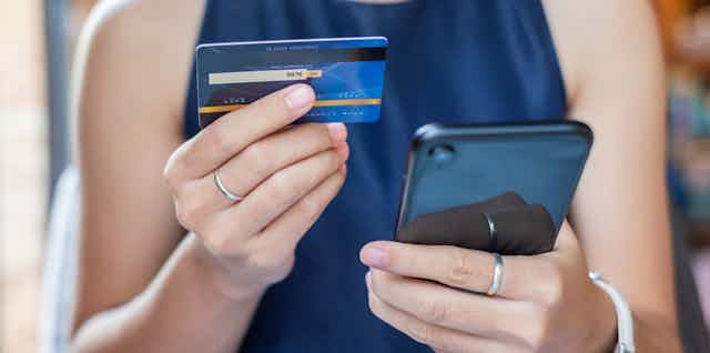 A woman holds a credit card in one hand and a smart phone in the other